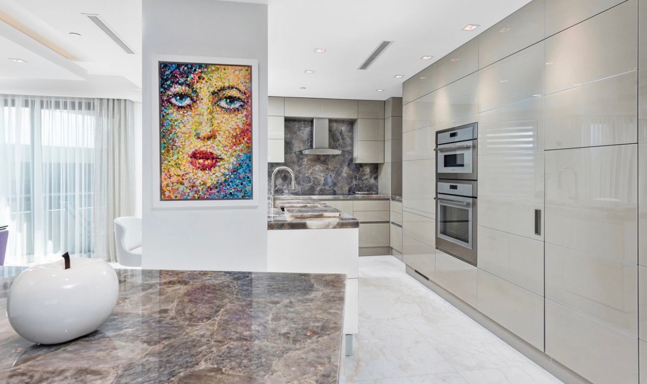 Contemporary kitchen with glossy cabinetry, stone counters, and colorful artwork